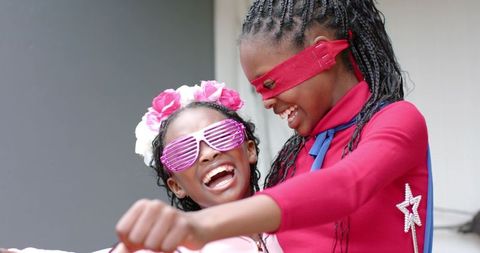 African american girls laughing, playing superheroes with capes, masks and shutter shades