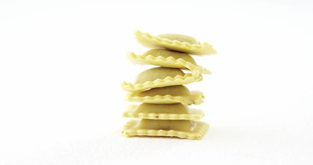 Stacked ravioli pasta is neatly arranged against a white background, with copy space. This simple composition emphasizes the shape and texture of the Italian cuisine staple.
