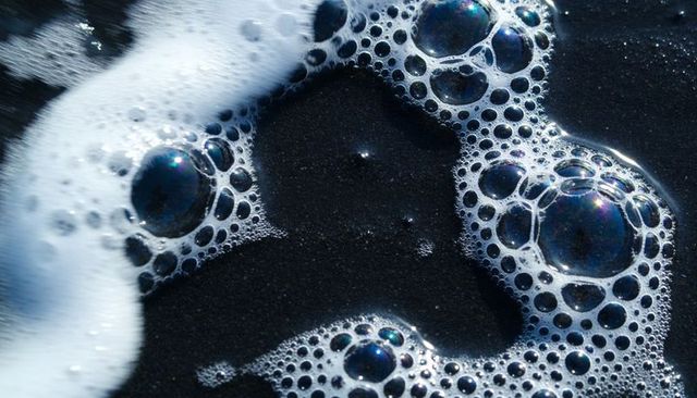Iridescent sea foam bubble chain on black sand macro close-up texture