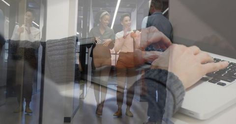 Hands typing overlaying colleagues walking through glass corridor modern open-plan workplace