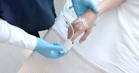 Healthcare Professional Adjusting Finger Oximeter on Patient's Hand