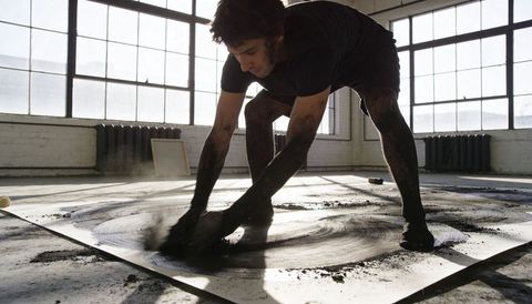 Contemporary artist creating large-scale charcoal spiral on floor of sunlit loft