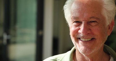Senior Man Smiling Comfortably Indoors Near Sunlit Glass Doors