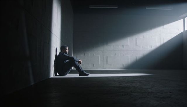 Solitary man sitting in industrial concrete space under dramatic high window beam