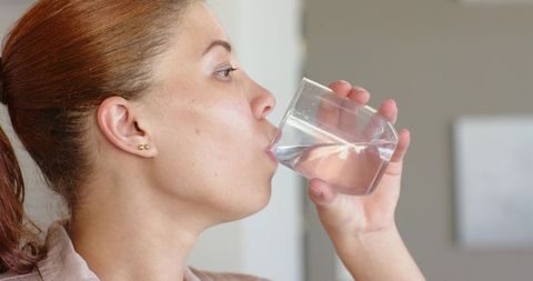 Young woman drinking water from faceted glass in office profile wearing gold studs