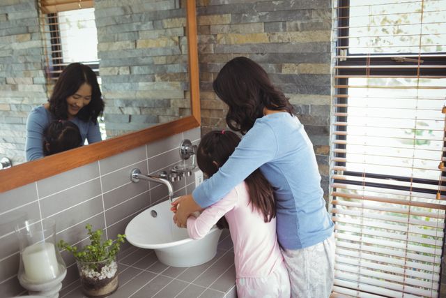 Mother and daughter washing hands in bathroom sink at home