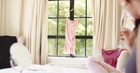 Pale pink slip dress hanging at sunlit black-framed bedroom window