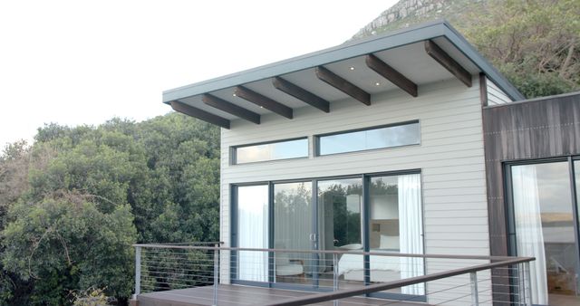Beautiful modern tiny house with sleek lines, large glass windows and a balcony amidst a scenic natural backdrop. Ideal for lifestyle magazines, architectural presentations, real estate listings, and design inspiration.