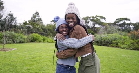 African American Girls Hugging in Garden Wearing Knit Hats and Braids, Outdoor Friendship