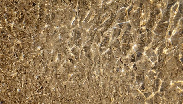 Shimmering golden caustics and rippled metallic texture with sparkling highlights closeup