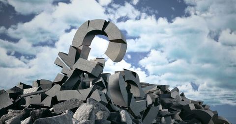 Giant broken question mark on rocky terrain under cloudy sky