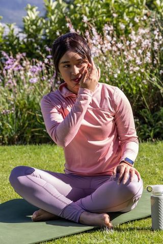 Asian woman practicing outdoor yoga sitting cross-legged on mat in pink activewear