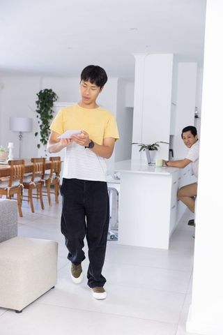 Asian roommates using tablet in modern bright open-plan kitchen with greenery casual lifestyle