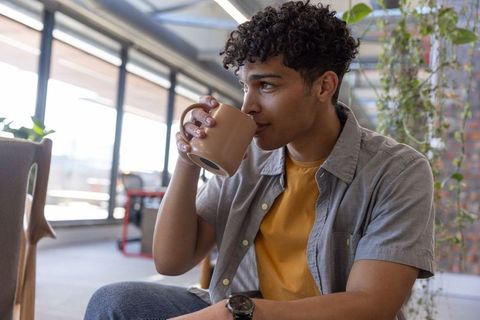 Young Man Enjoying Coffee in Modern Cafe with Greenery