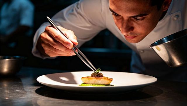Chef delicately plating seared fish with caviar and microgreens for fine dining service