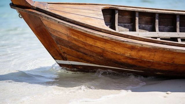 Varnished wooden boat bow resting on tropical sand with gentle waves lapping hull