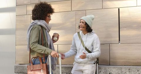 Diverse female friends chatting outdoors with suitcases and coffee while traveling