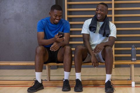African american friends laughing on gym bench checking smartphone after workout