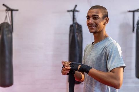 Young boxer wrapping hands by heavy bags in gym preparing for training session