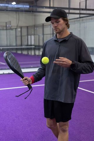 Male athlete practicing padel on purple indoor court with paddle and yellow ball