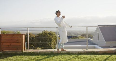 Mid-adult asian woman in white bathrobe enjoying morning coffee on rooftop terrace