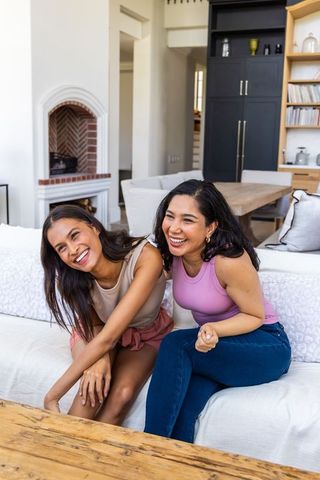 Two diverse women laughing on white sofa in bright modern living room