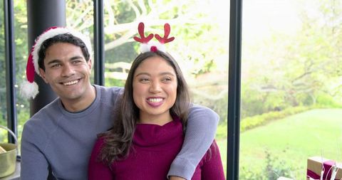 Smiling couple celebrating cozy holiday at home wearing Santa hat and reindeer antlers