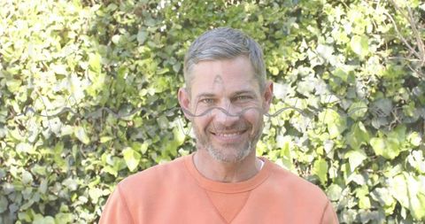 Smiling Middle-Aged Man Wearing Orange Sweatshirt in Sunlit Ivy Garden Background