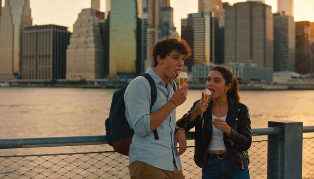 Young couple enjoying melting ice cream cones at riverside with urban skyline at sunset