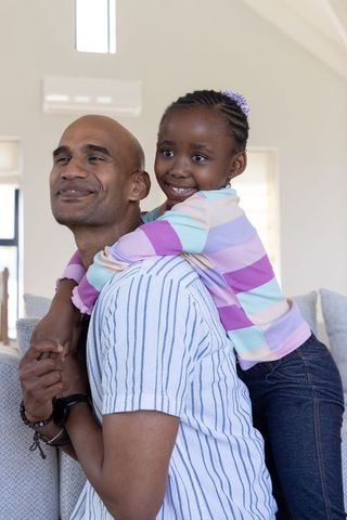 African american father giving daughter piggyback hug sharing laughing moments at home