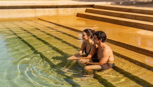 Young couple relaxing on submerged pool steps in terracotta terrace under warm sunlight