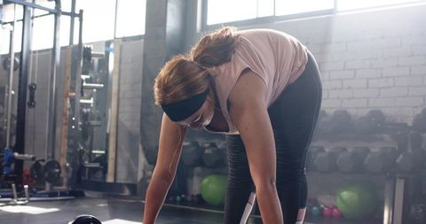 Mid adult woman reaching for kettlebell in industrial gym backlit by daylight