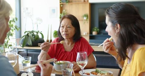 Multigenerational women sharing home-cooked asian meal with chopsticks around dining table