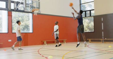 Diverse men practicing basketball drills and shooting jump shots on bright indoor court