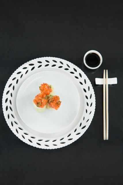 This image showcases a beautifully plated serving of steamed dumplings on an elegant white plate, accompanied by chopsticks and a small dish of soy sauce. The minimalist presentation with a black background highlights the vibrant colors of the dumplings, making it perfect for use in food blogs, restaurant menus, culinary magazines, and Asian cuisine promotions.