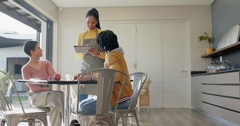 Cafe server using tablet taking order from smiling guests in modern industrial kitchen natural light