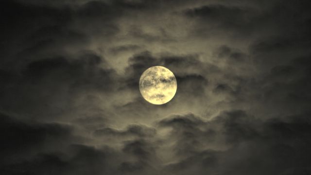 Full moon glowing amidst dark clouds suggesting an eerie and mysterious atmosphere. Ideal for use in themes related to astronomy, night sky studies, celestial events, or creating a dramatic and spooky ambiance in Halloween designs and Gothic-themed projects.