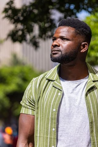 African man standing in sun looking upward wearing green striped shirt and gray tee