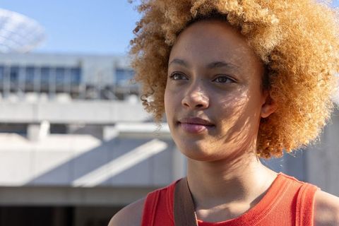 Young african american woman gazing in sunlight with curly blonde hair and red top