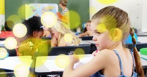 Focused elementary girl looking across classroom while classmates whisper, soft bokeh glow