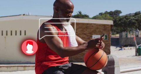 Senior athlete checking phone while resting with basketball on seaside promenade near beach