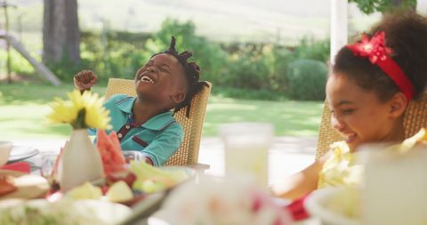 Happy diverse brother and sister laughing at family dinner table in sunny garden - Download Free Stock Photos Pikwizard.com