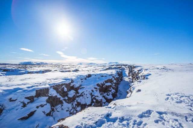 Snow covered landscape depicting a vast, frozen canyon under a bright sun and clear blue sky. The terrain is snow-capped with stunning contrasts between white snow and rocky surfaces. This image perfect illustrating the beauty and tranquility of winter scenery. Ideal for use in travel websites, adventure tourism promotions, and nature conservancy projects highlighting winter destinations and natural beauty.