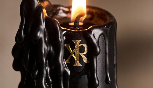 Burning black pillar candle melting glossy wax drips with gold monogram emblem