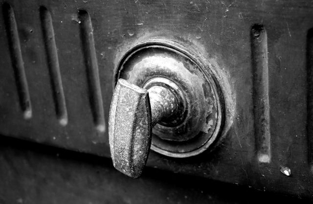 This image shows a close-up view of an old, rusty metal door handle in black and white. It highlights the texture and age of the metal, making it suitable for use in historical content, themes of aging or decay, or for vintage decor inspiration.