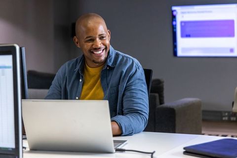 African american man smiling at laptop in modern collaborative office with monitors