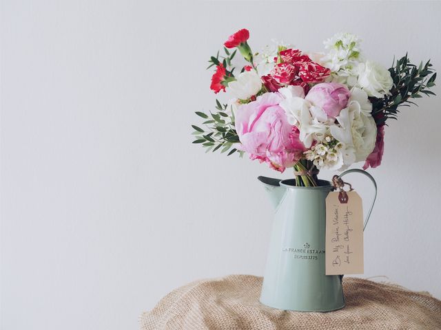 Floral bouquet in a pastel jug, placed on burlap fabric, is a stunning display of vibrant spring flowers like peonies and carnations mixed with greenery. Perfect for use in home decor, holiday greetings, floral arrangement promotions, or interior design blogs.