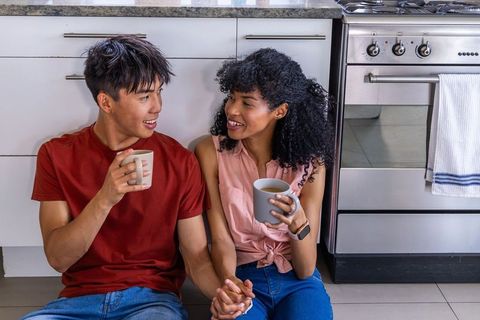 Mixed-race couple sharing coffee and holding hands while sitting on kitchen floor