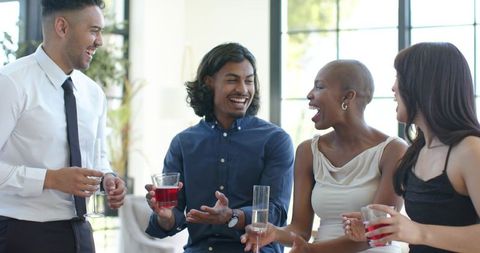 Smiling diverse young professionals laughing, networking with cocktails in bright lounge