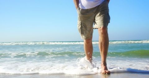 Senior Enjoys Relaxing Walk on Sunlit Beach at Shoreline